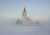 Local church in village Spodnji Brnik, Slovenia after sun went down on snow covered fields. After cold day, fog starts to form over fields covered with snow, giving winter landscape unique mysteriousness.